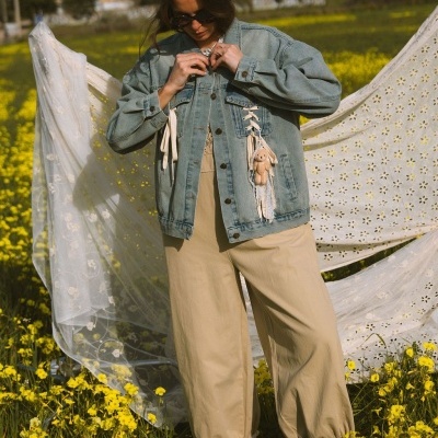 Mulher com casaco de ganga azul claro e calças largas bege num campo florido amarelo