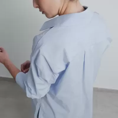 Mulher com camisa azul clara e calças cinza de padrão sutil em ambiente interior