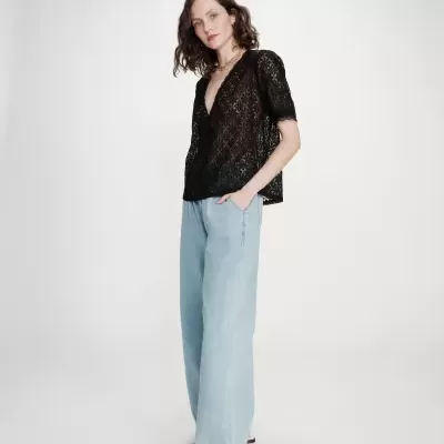 Mulher com blusa preta de renda e calças de ganga largas azuis