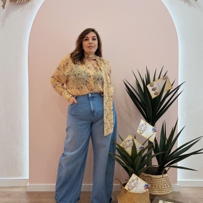 Mulher com blusa floral amarela, calças de ganga largas azuis e sapatos bege com plantas e cartas postais