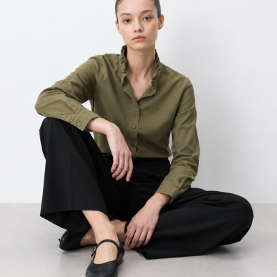 Mulher com camisa verde oliva e calças pretas sentada no chão
