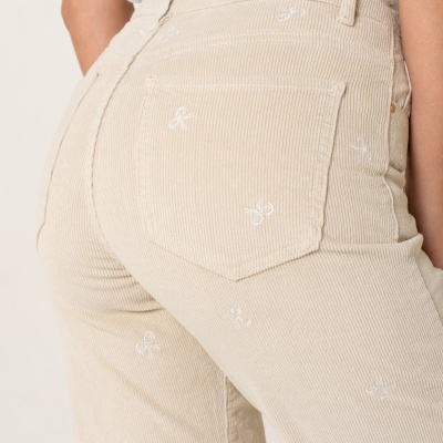 Calças de veludo cotelê bege com bordados brancos de laço na parte de trás.