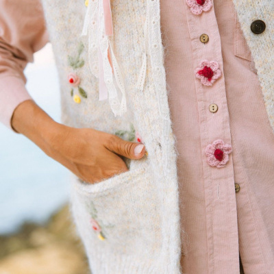 Colete de malha bege com bordados florais e camisa rosa com botões florais