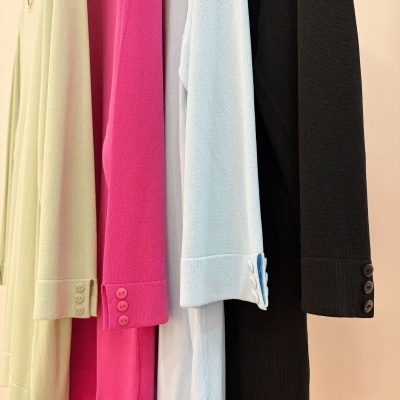 Casacos de malha em creme, rosa, azul claro e preto pendurados com botões nos punhos.