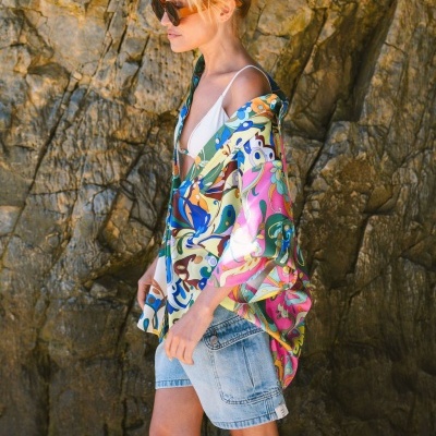 Mulher com camisa multicolorida e shorts de ganga junto a rochas