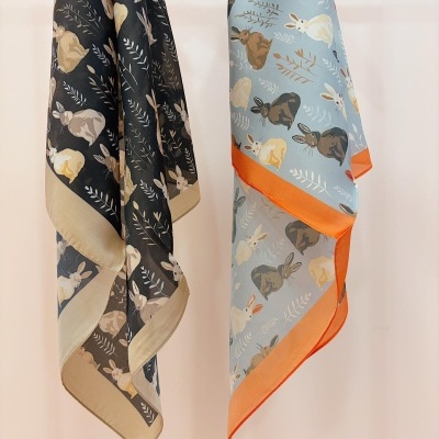 Dois lenços com padrão de coelhos e folhas, fundo preto e azul claro, bordas bege e laranja.