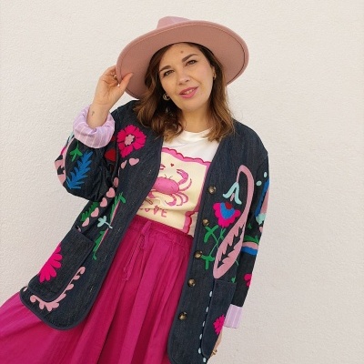 Mulher com chapéu rosa, casaco bordado colorido, t-shirt com caranguejo e calças fúchsia