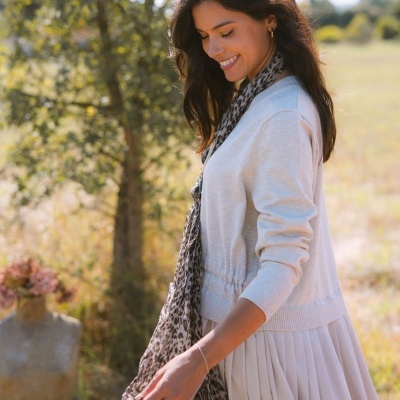 Mulher com cardigan bege claro, saia plissada e cachecol animal print ao ar livre