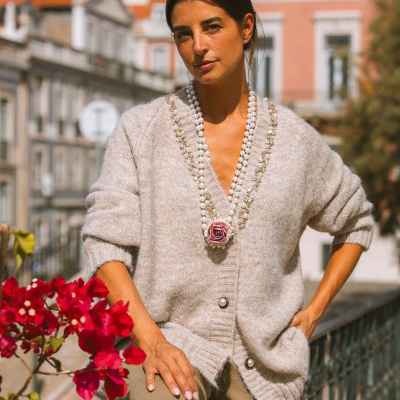 Mulher com camisola cinza clara de malha e colar de pérolas com pingente rosa
