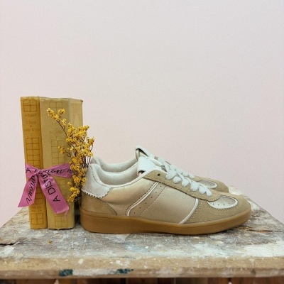 Sapatilhas bege e branco junto a livros amarelos com fita rosa numa mesa de madeira