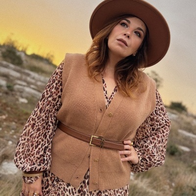 Mulher com chapéu castanho, vestido animal print e colete de malha castanho