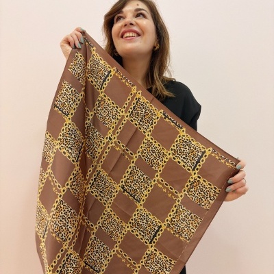 Lenço quadrado castanho com padrão de correntes douradas e animal print segurado por mulher