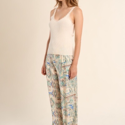 Mulher com camisola de alças creme e calças largas estampadas coloridas