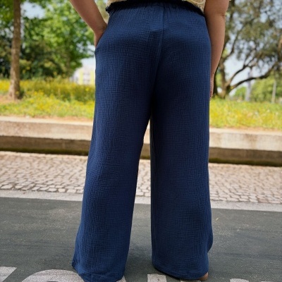Calças largas azul escuro com cintura elástica, vistas de costas, usadas com blusa amarela bordada em parque exterior