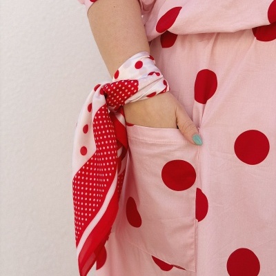 Braço com vestido rosa de bolinhas vermelhas e lenço branco com bolinhas vermelhas amarrado no pulso
