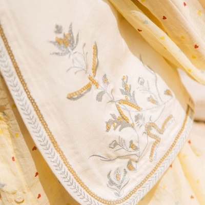 Lenço branco bordado com padrão floral em tecido sobre roupa amarela com corações coloridos.