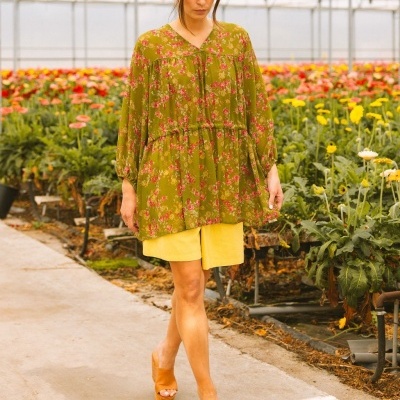 Blusa feminina verde floral com calções amarelos e sandálias castanhas num viveiro de flores