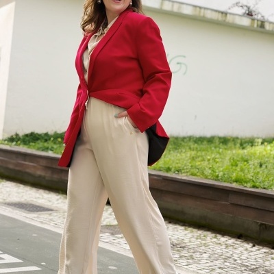 Mulher com blazer vermelho e calças largas bege a andar na rua