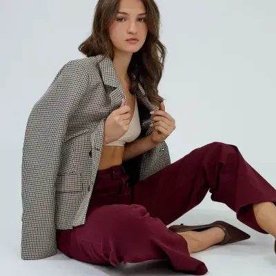 Mulher com blazer aos quadrados, top bege, calças vinho e sapatos castanho sentada