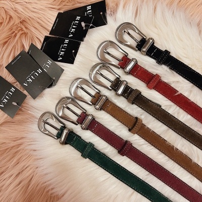 Sete cintos de couro coloridos com fivelas prateadas e etiquetas da marca RUIKA sobre tapete peludo branco e rosa