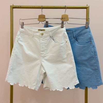 Dois calções de ganga branco e azul com bordado floral pendurados num cabide de metal e madeira