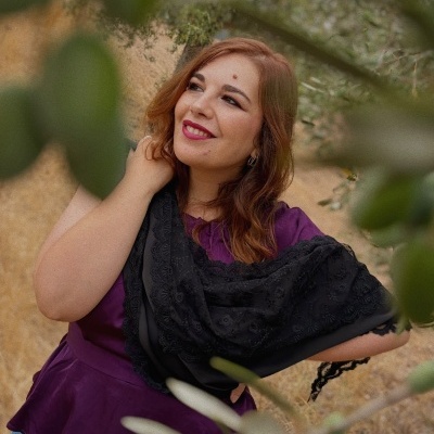 Mulher com blusa roxa e lenço preto bordado em ambiente natural