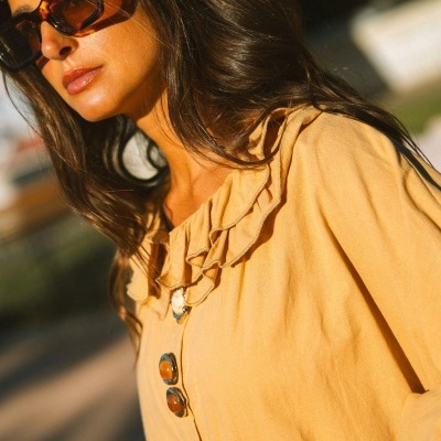 Blusa mostarda com botões grandes e gola com folhos usada ao ar livre.