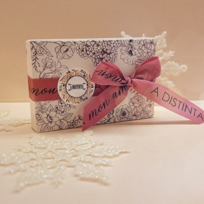 Caixa decorativa branca com padrão floral preto e laço rosa com texto em fundo bege
