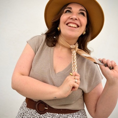 Mulher sorridente com roupa bege, chapéu castanho e lenço ao pescoço
