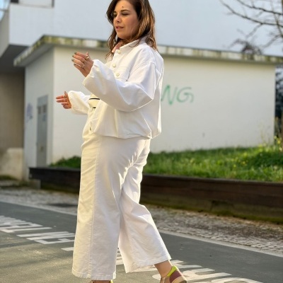 Mulher vestindo casaco e calças brancas com sapatilhas castanhas e amarelas ao ar livre