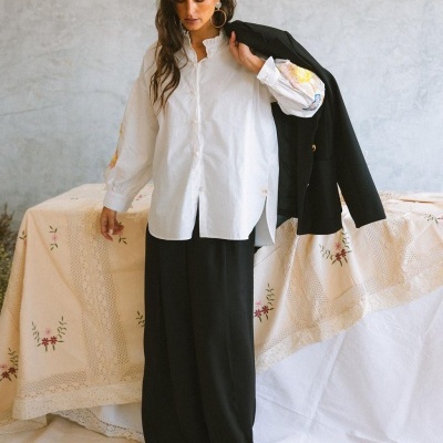 Mulher com camisa branca bordada e calças pretas segurando blazer preto