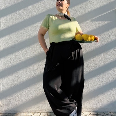 Mulher com blusa verde, calças pretas e lenço ao pescoço segurando prato com limões