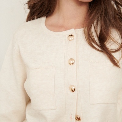 Camisola cardigã creme com botões dourados e bolsos frontais, detalhe superior de mulher