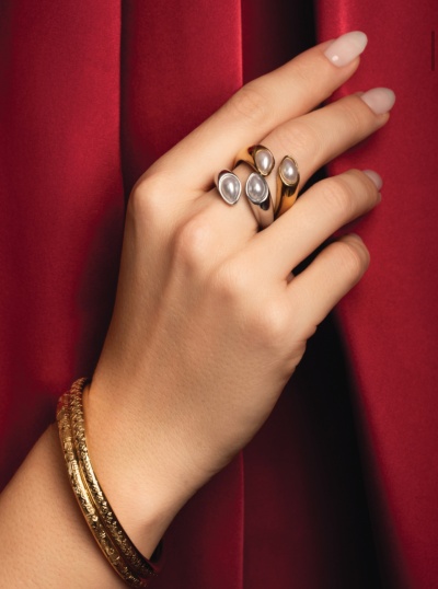 Mão com anéis de pérola e pulseiras douradas em fundo vermelho