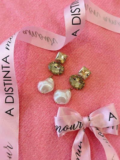 Brincos com pedras douradas e pérolas sobre fundo rosa com fita