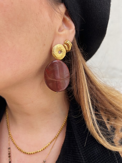 Brinco pendente com pedra castanha e base dourada num pescoço feminino