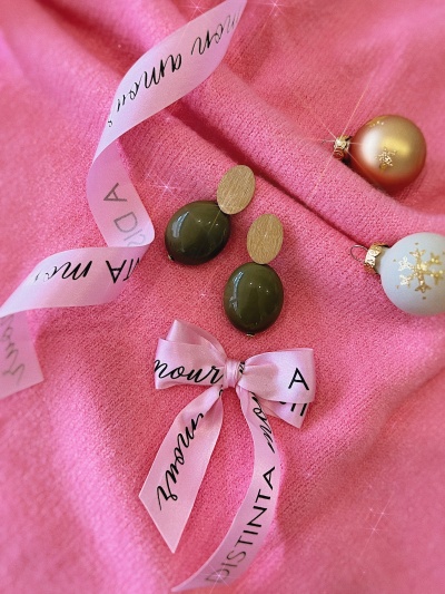 Brincos dourados e verdes com fita rosa e bolas de Natal sobre tecido rosa