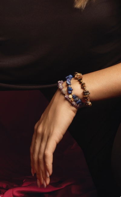 Pulso com 3 pulseiras de pedras naturais coloridas em fundo escuro