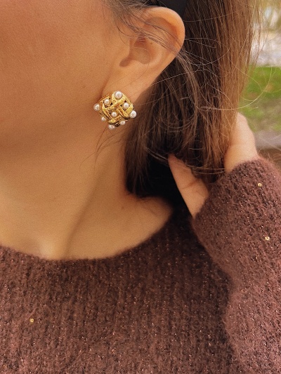 Brinco dourado com pérolas usado por pessoa com pulôver castanho