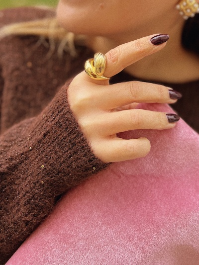 Mão com anel dourado e camisola castanha com lantejoulas sobre tecido rosa.