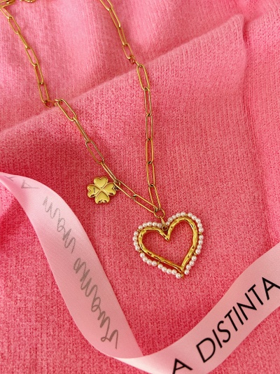 Colar dourado com pendente de coração e trevo sobre fundo rosa