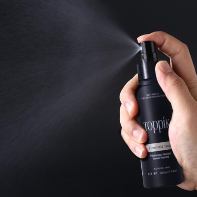 Mão a pulverizar spray Toppik Fiberhold em frasco preto