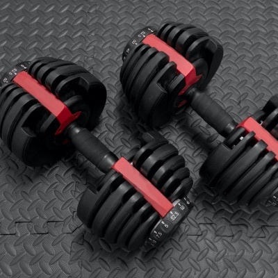Par de halteres ajustáveis preto e vermelho sobre piso de borracha preto com padrão de losangos