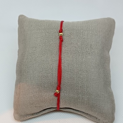 Almofada cinza com pulseira vermelha com detalhes dourados