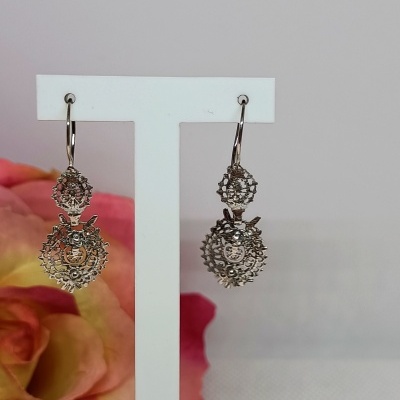 Brincos pendentes prateados em suporte branco com flor cor de rosa ao fundo