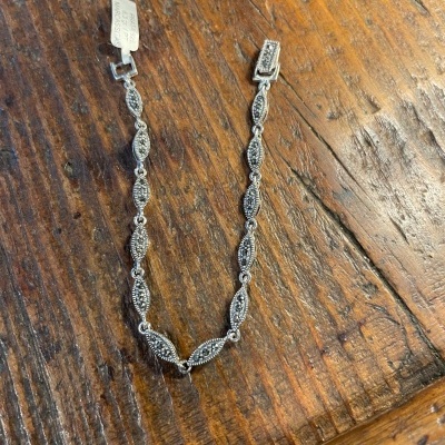 Pulseira de prata com detalhes pretos sobre mesa de madeira