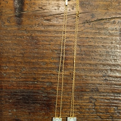 Dois colares dourados com pendentes retangulares gravados sobre madeira rústica