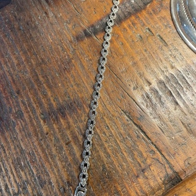 Pulseira em prata com elos entrelaçados sobre mesa de madeira