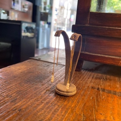 Brincos dourados com pérolas em suporte cinzento sobre mesa de madeira