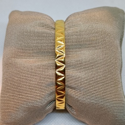 Pulseira dourada com padrão geométrico exposta numa almofada bege